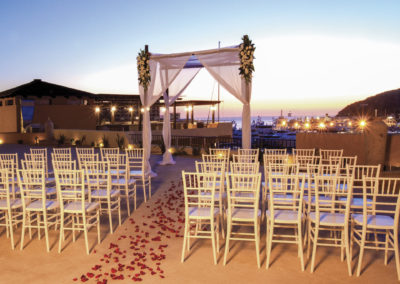 A wedding ceremony with white chairs and red rose petals.